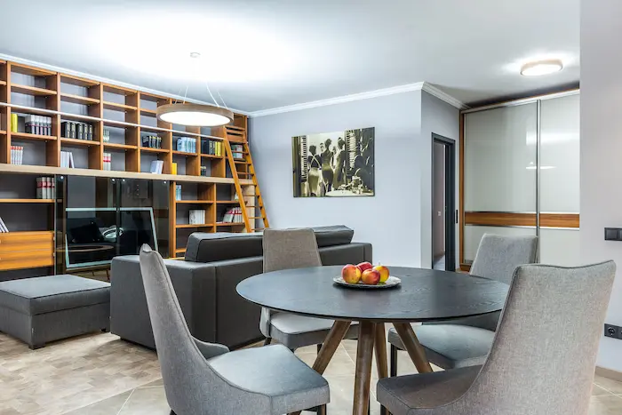 Salon moderne avec canapé gris, table ronde noire et bibliothèque boisée, illustration d’un intérieur bien meublé et chaleureux.