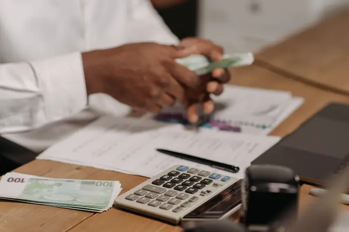 Personne comptant billets d’euros sur bureau avec calculatrice et documents, reflet d’une gestion liée à un emprunt bancaire.