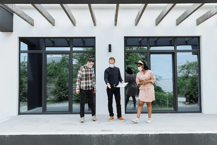 Trois personnes discutant devant immeuble moderne, image illustrant l’achat d’un appartement neuf pour un investissement locatif.
