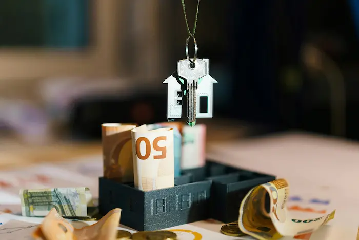 Clé argentée suspendue au-dessus d’une maison miniature remplie de billets, image illustrant le crédit-bail immobilier et l’investissement locatif.