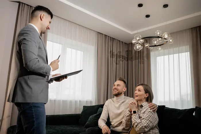 Trois personnes en salon moderne discutant devant canapé vert, reflet d’un rendez-vous lié à un achat immobilier.