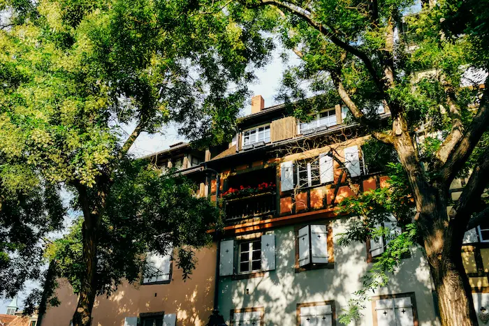 Façade d’un bien immobilier charmant entouré de verdure, balcon fleuri et architecture traditionnelle offrant une atmosphère paisible et accueillante.