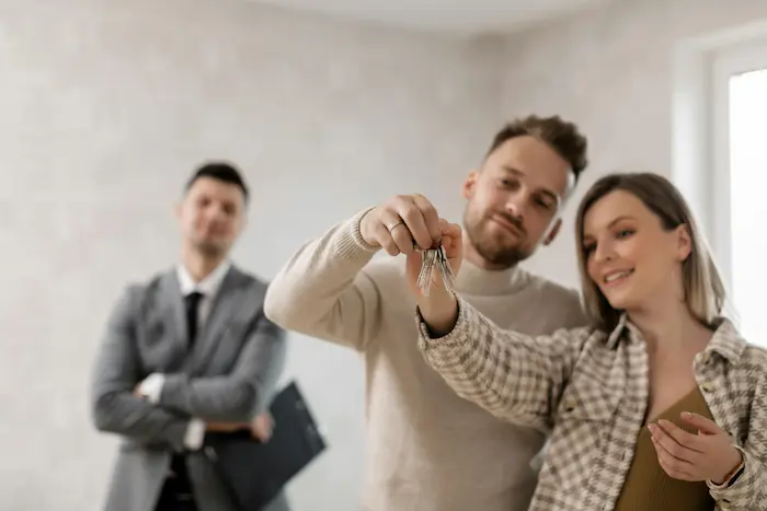 Deux personnes tenant clés devant conseiller en costume, image illustrant le rôle du courtier en prêt immobilier pour accompagner l’achat.