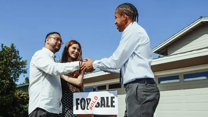 Trois personnes devant une maison, poignée de main et panneau vendu, illustrant la relance logement par l’accès facilité à la propriété.