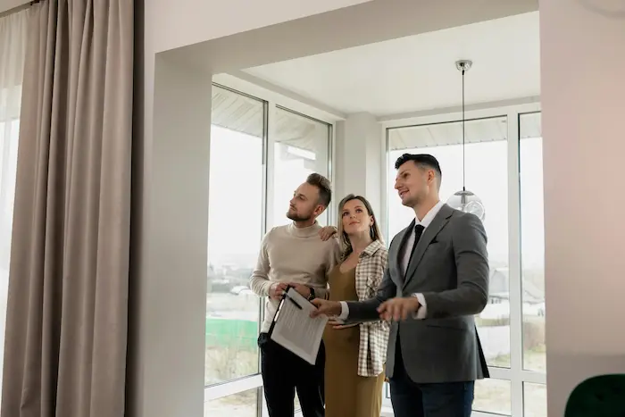 Trois personnes dans salon lumineux avec grandes fenêtres, image illustrant achat résidence principale et découverte d’un bien immobilier.