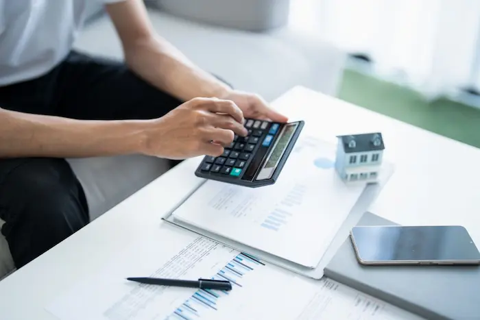 Main manipulant calculatrice près d’une maison miniature, image représentant le calcul de la taxe foncière.
