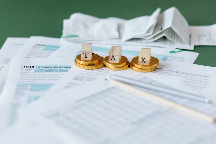 Formulaire fiscal américain posé sur bureau avec pièces et mot TAX en blocs, image qui illustre l’acte de déclarer ses impôts.