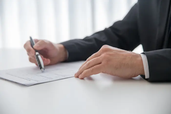 Scène de bureau où un homme en costume remplit sa déclaration d’impôt, stylo en main et document imprimé devant lui.